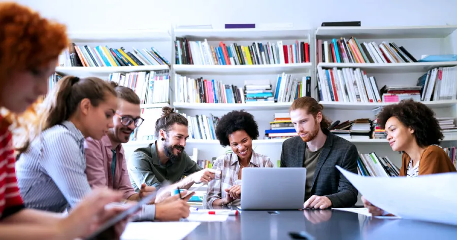 a group of people sitting around a table looking at a laptop.