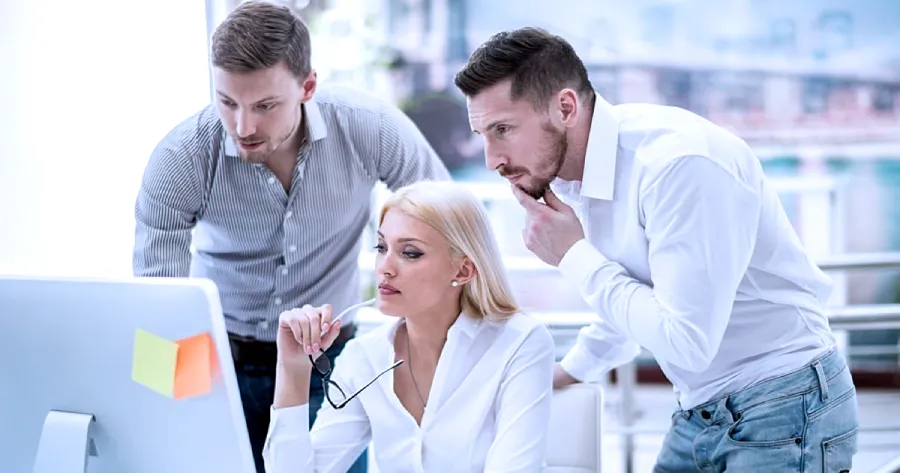 An team of professionals ( 2 men and a woman) are looking at a desktop computer. 