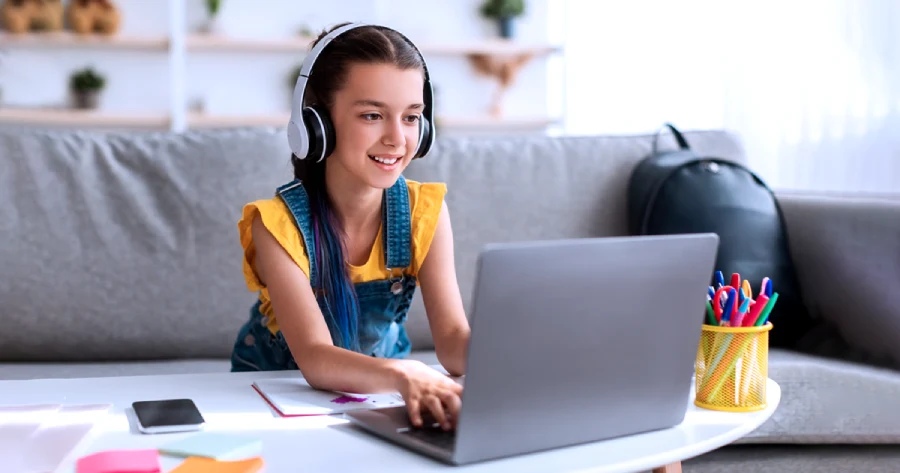 A girl with headphones is attempting an adaptive assessment on a laptop. 