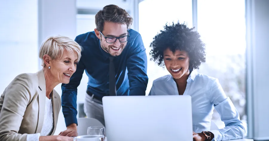 2 women and 1 man are looking at a laptop screen. 