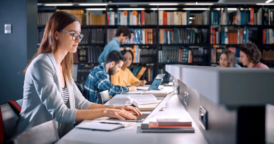 A girl studying on a laptop in a library.