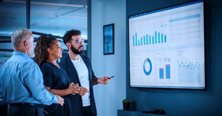  A team of 2 men and a woman are looking at analytics on a screen. 