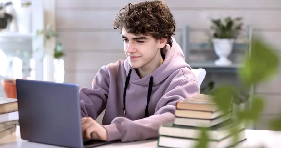 A young male smiling and working on a laptop. 