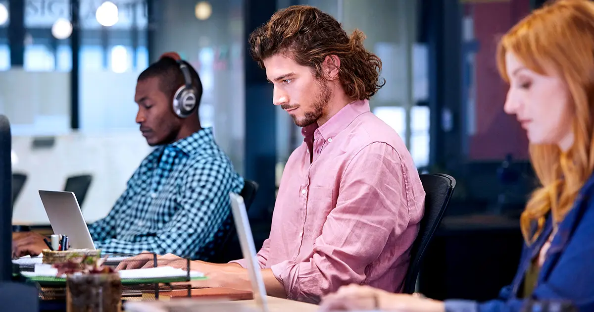 A man and a woman sitting on a desk working on a laptops. 