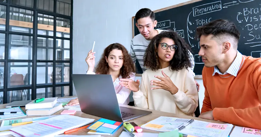 4 students sitting in front of a laptop, discussing.