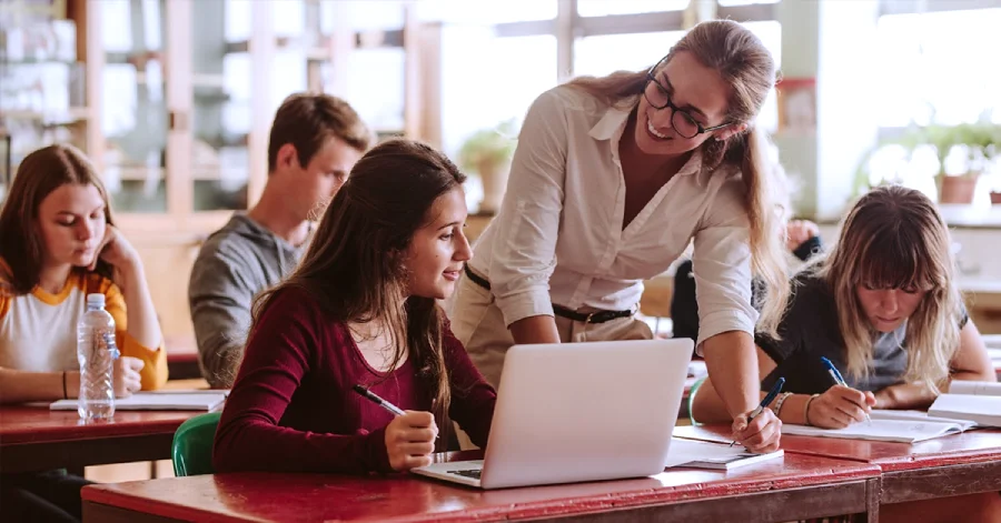 A teacher standing next to a student in a classroom.