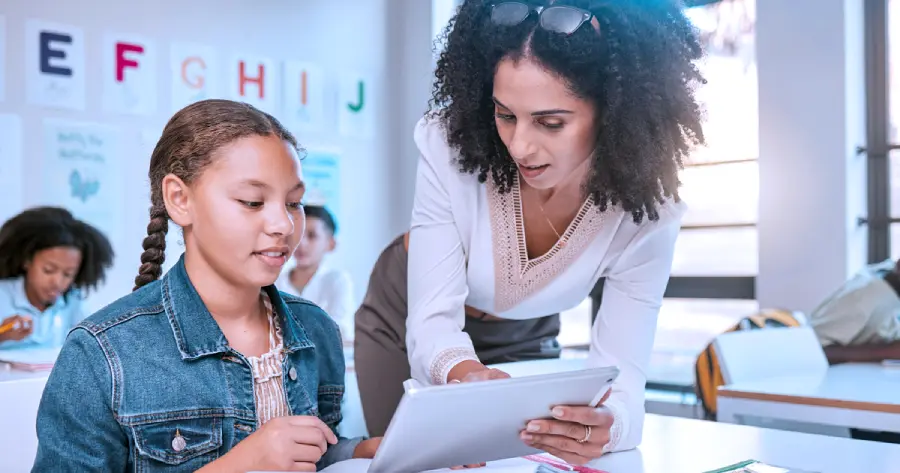 A female teacher teaching a female student on a tablet. 