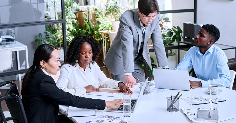 Corporate professionals, with one being disabled, discussing accessibility policy and reports.
