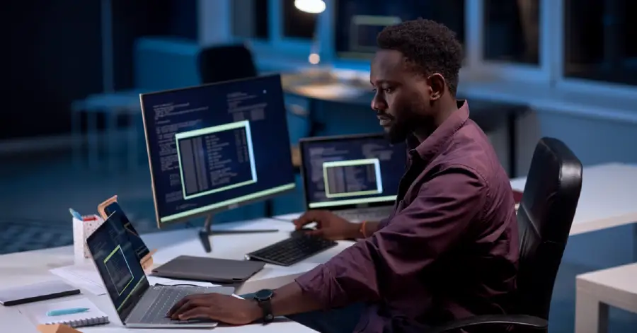 A man sitting at a desk analyzing AI in Education data on multiple computers. 