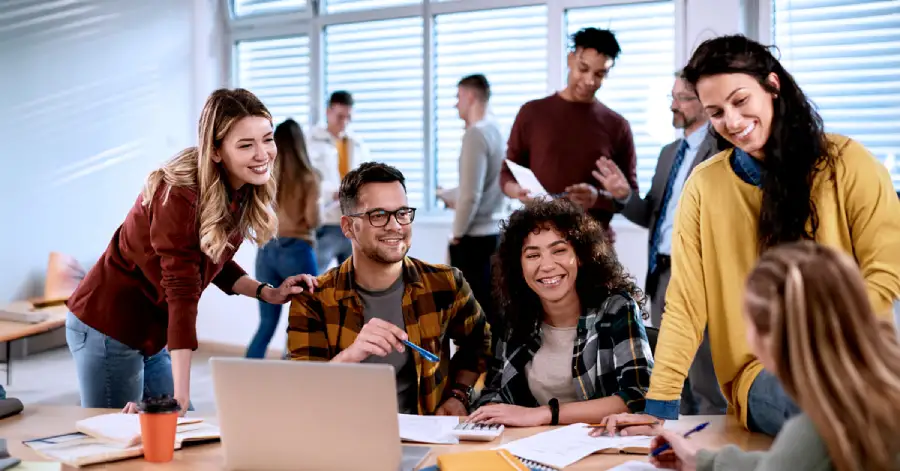 A multi-ethnic group of university students excitedly discuss AI in higher education while learning together in a bright classroom.