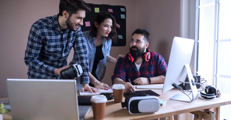 Three cheerful young developers are huddled together, working on a new immersive learning program.