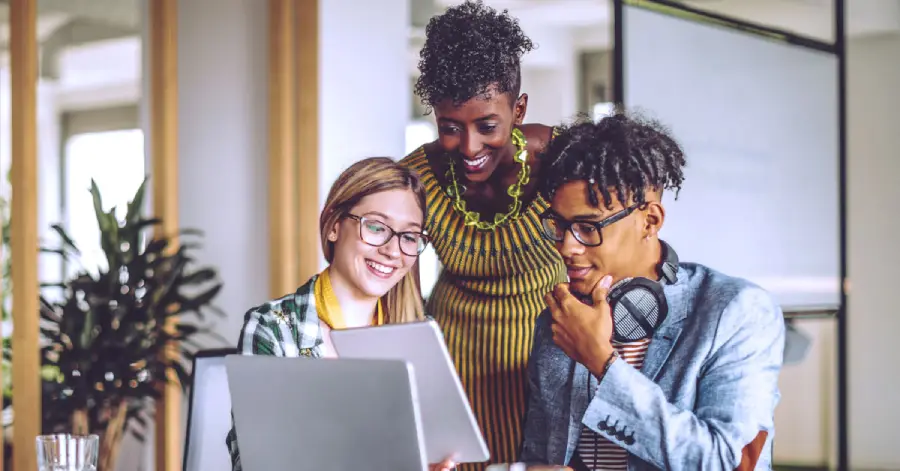  Three colleagues collaborating over a laptop in a modern office discussing the role of AI in education.