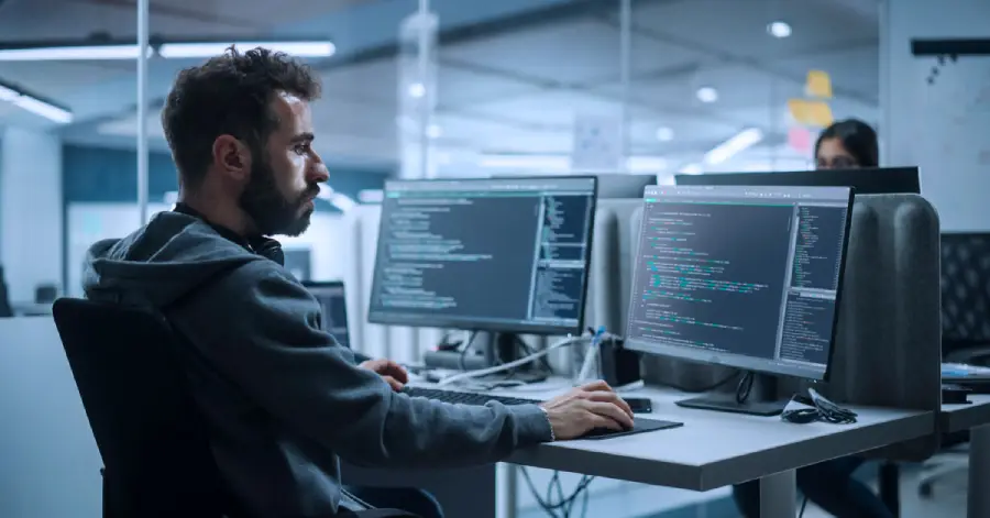 A man sitting at a desk in front of two computer monitors working on AI tools in education.