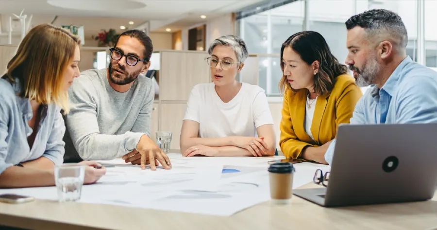 A diverse group of people sit around a table, engaged in a discussion about accessibility. 