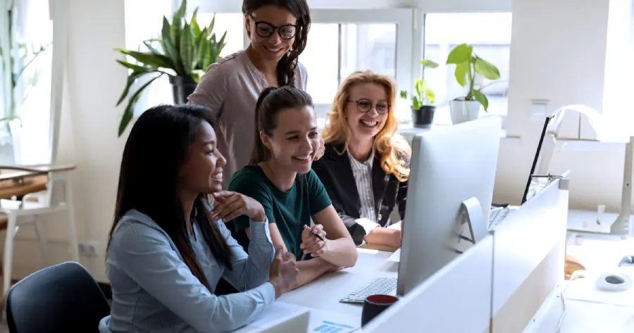 Four women working together in a bright office setting, looking at a computer screen and reading the latest Learning and Development trends.