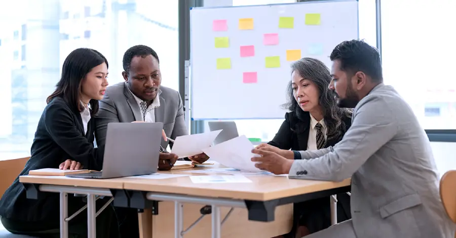 A group of multi-racial corporate professionals discussing with each other the accessibility implications of web accessibility audit tools.
