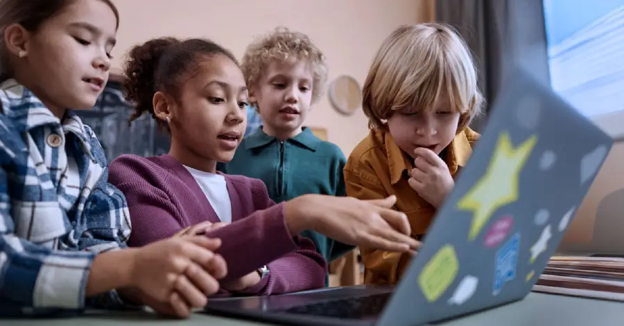 A diverse group of school students sitting in front of a laptop and learning about custom content development in education. 