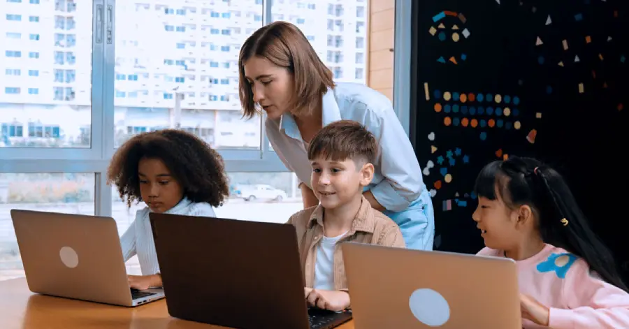  A female teacher is assessing the work of students, sitting in front of their laptops based on the custom content development in education.